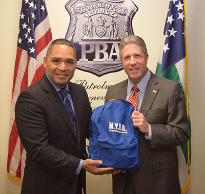 NYDO President Lt. Angel Fermin (left) and PBA President Patrick J. Lynch (right) holding the NYDO school supply bag that will be distributed on the trip. (Photo Credit: NYC PBA). 